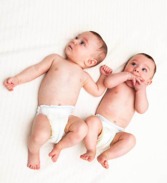 istock Identical twin baby boys in diapers looking away on white 1004835990
