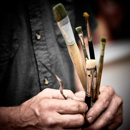 artist holding palette knife and paintbrush in studio