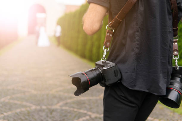 Professional wedding photographer takes pictures of the bride and groom in garden, the photographer in action with two cameras on a shoulder straps. stock photo