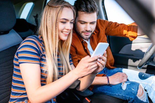 istock smiling young couple sitting in car and looking at smartphone screen 1004889622