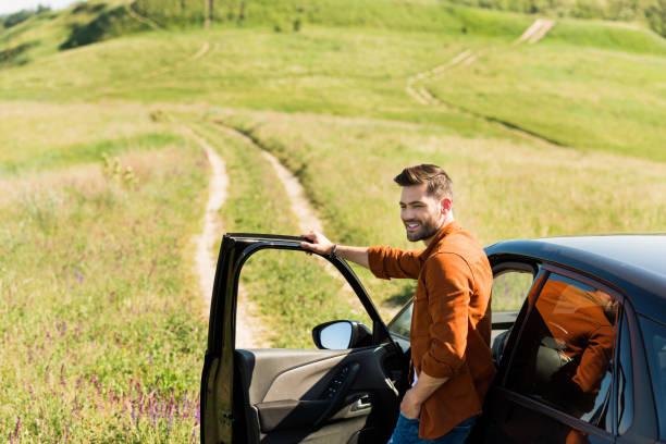 istock young smiling man standing near car on rural meadow 1004889710