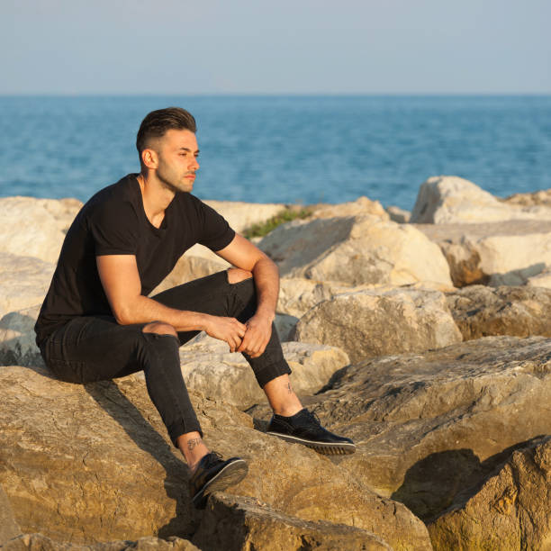 istock Thoughtful Young Man Sitting On Rock By Sea Against Sky 1004898078