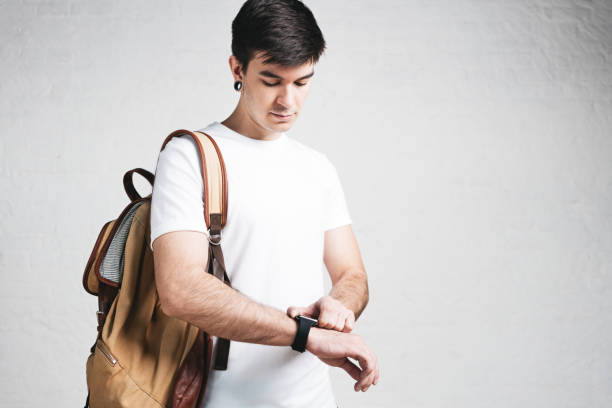 istock Young athletic man wearing blank white t-shirt, backpack and smartwatch, studio close-up, empty wall 1004915294