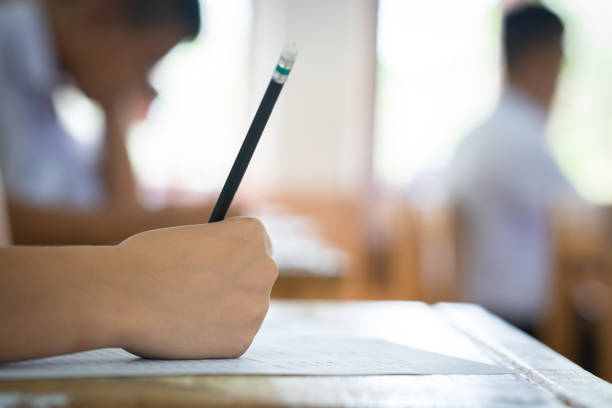 Student holding pencil writing answer of question on paper test examination stock photo