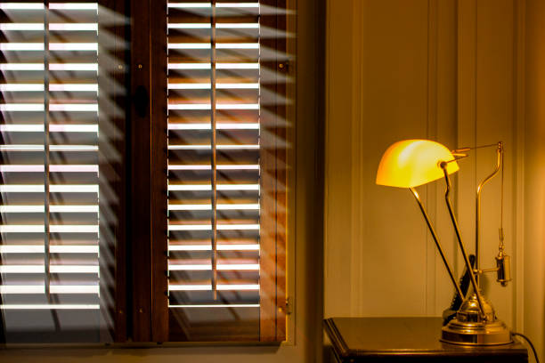 istock sunshine coming through plantation shutters compete with light from a brass lamp against painted panelling Normandy style, French 1004952692