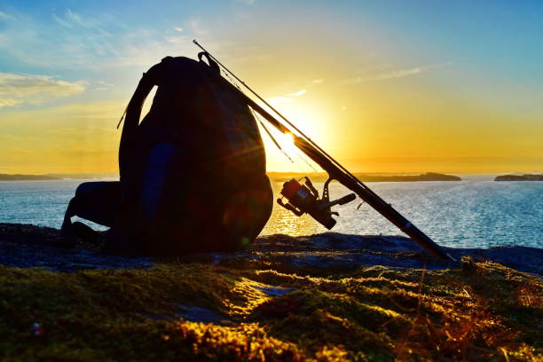silhouette of a backpack and fishing rod against the rising sun and the sea