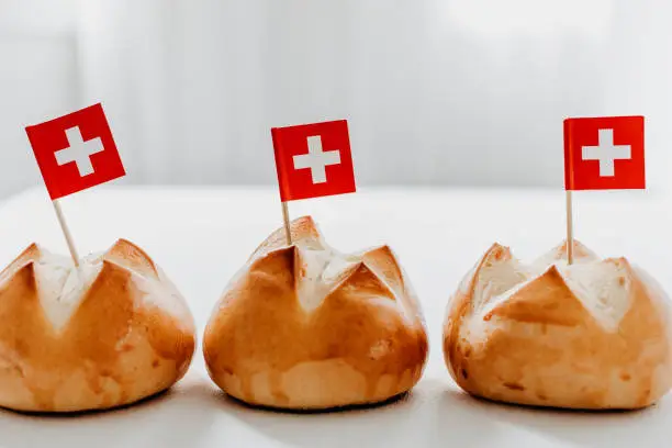 Traditional swiss bread buns called in German 1.Augustweggen baked in Switzerland to celebrate Swiss National Day on August 1st. The top of the bread being cut crosswise to shape a cross as symbol of Switzerland. Swiss flags on wooden toothpicks.  White background, isolated, copy space.