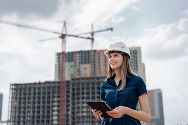 ingénieur en construction femelle. l’architecte avec une tablette pc à un chantier de construction. jeune femme à la recherche, site lieu s’appuyant sur le fond. concept de construction - architect female women construction photos et images de collection