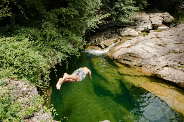 istock Young Adult Man Jumping in a Stream Pool from a Rock 1005008968