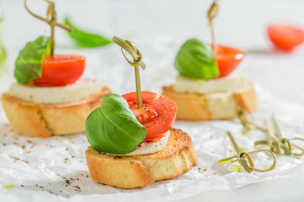 closeup de crostini com mussarela e tomate em papel branco - bruschetta cutting board italy olive oil - fotografias e filmes do acervo
