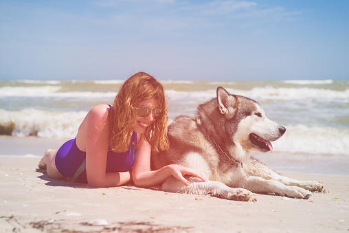 Young smiling female and dog laying at sand near sea