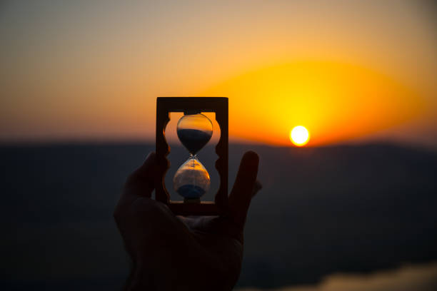 istock Life time passing concept. Hand holding hourglass with sunset sky background. 1005086108