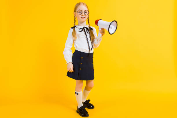 Girl with red pigtails on a yellow background. A charming girl in round transparent glasses is holding a loudspeaker in her hands. Portrait of a beautiful girl in a white blouse and black skirt. see through leggings stock pictures, royalty-free photos & images