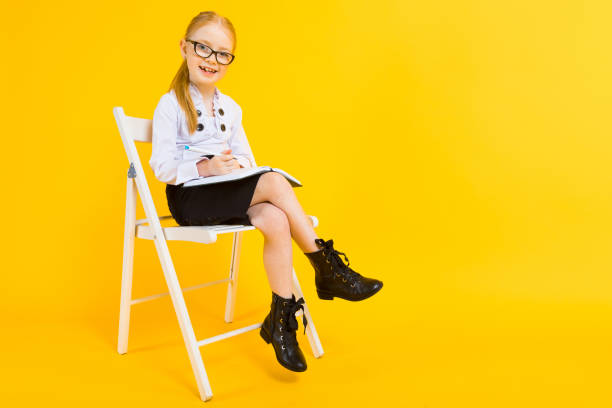Girl with red hair on a yellow background. A charming girl in transparent glasses sits on a white chair and makes notes in a notebook. Portrait of a beautiful girl in a white blouse and black skirt. see through leggings stock pictures, royalty-free photos & images