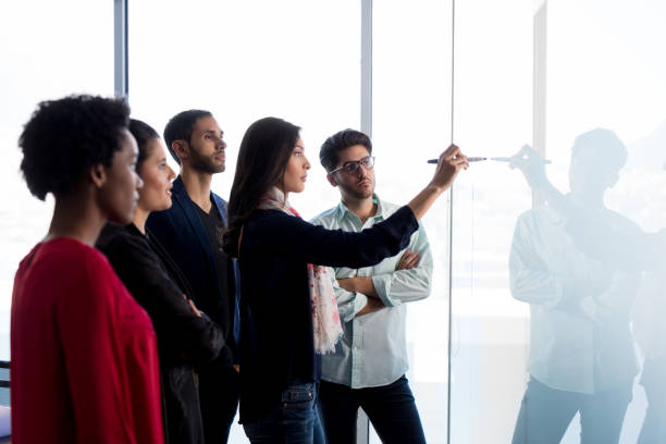 istock Young woman writing on glass wall and colleagues looking 1005123940