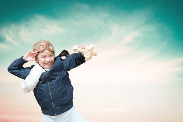Kid playing with toy airplane. Children dream of travel by plane. Happy child girl has fun in summer vacation by sea and mountains. Outdoors activities at background of blue sky. Lifestyle moment.