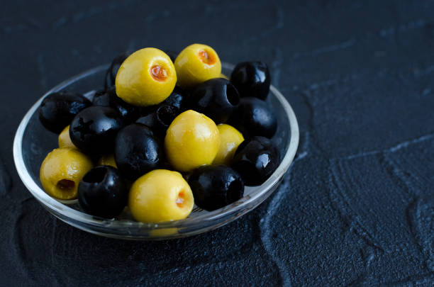 Black and green olives in glass bowl on dark stone background. Copy space.