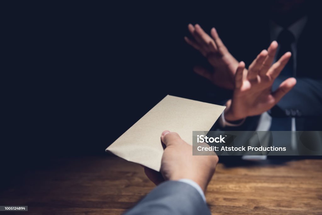 Businessman rejecting money in the envelope, anti bribery concept Businessman rejecting money in the envelope secretly offered by his partner in the dark for anti bribery concept Corruption Stock Photo