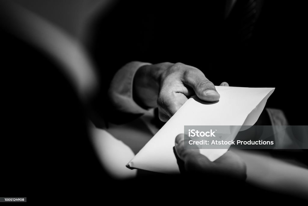 Businessman giving bribe money in the envelope to partner Businessman giving bribe money in the  envelope to partner in a corruption scam with black and white tone Corruption Stock Photo