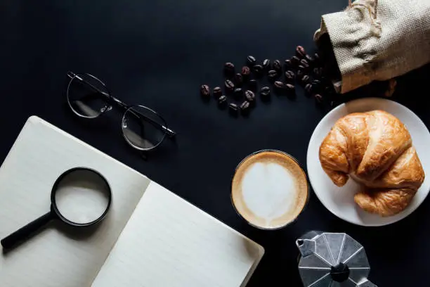 Latte art ,Croissant ,book,glasses and with Roasted coffee on black background in the morning top view and instagram style filter photo vintage tone