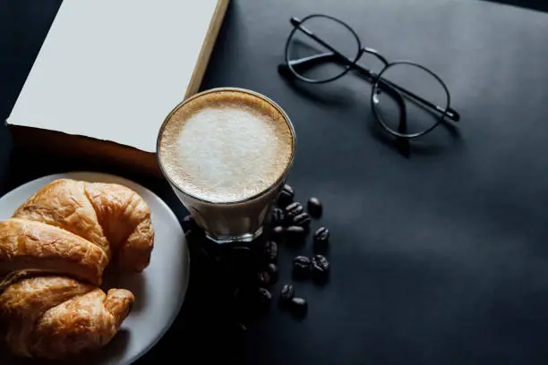 Latte art ,Croissant ,book,glasses and with Roasted coffee on black background in the morning top view and instagram style filter photo vintage tone