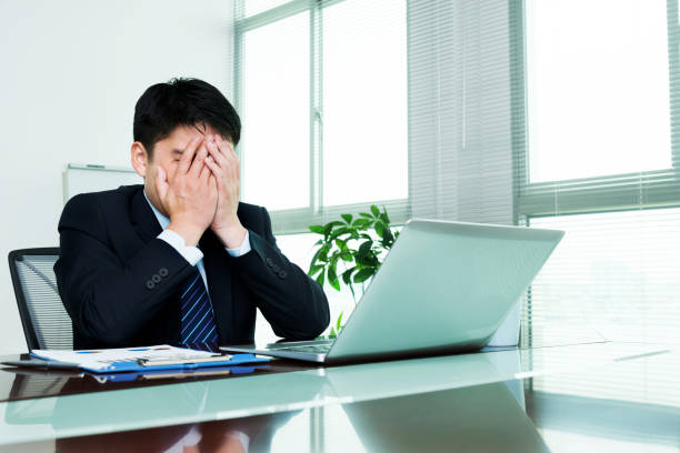 istock Tired businessman covering face at desk 1005246038
