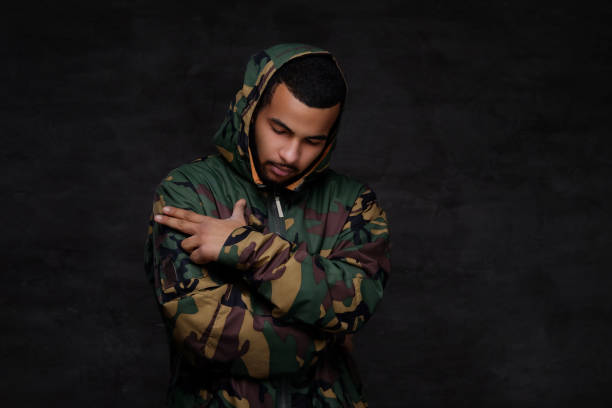 Handsome African-American guy wear military jacket. Handsome African-American guy wear military jacket. Isolated over dark background. camouflage rapper stock pictures, royalty-free photos & images