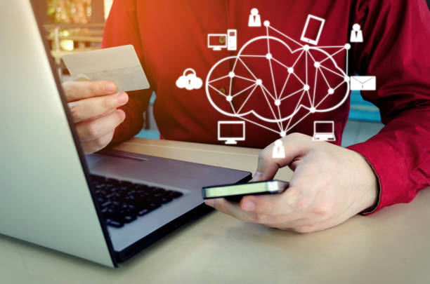 istock handsome man in red shirt paying with credit card and using smart phone with laptop computer on desk at home office and graphic network icon, payment and shopping online, lifestyle technology concept 1005257402