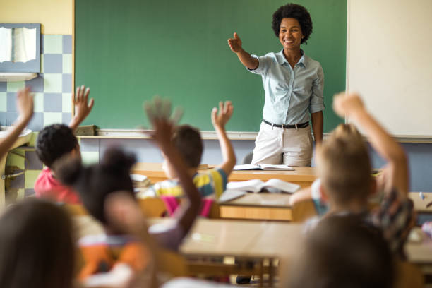 felice insegnante elementare afroamericana che mira a scolare per rispondere alla sua domanda. - studying child female student foto e immagini stock