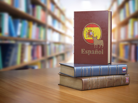 Learn Spanish concept. Spanish dictionary book or textbok with flag of Spain and cow on the cover in the library.