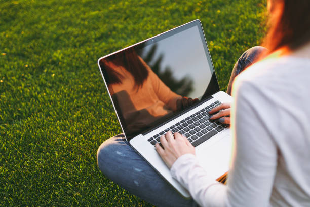 istock Close up hands on keyboard. Woman working on laptop pc computer with blank black empty screen to copy space in park on green grass sunshine lawn outdoors. Mobile Office. Freelance business concept. 1005324996