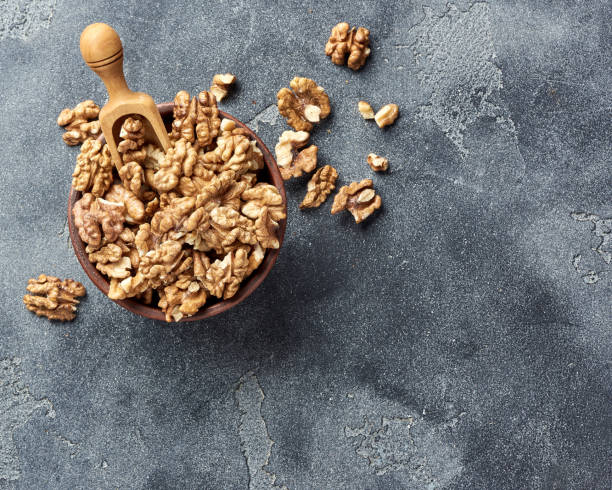 istock Walnut kernels with wooden scoop on gray background with copy space. Nuts in clay bowl. Top view. 1005330956