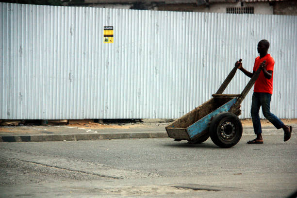 October 1st, 2012, Abidjan, Cote d'Ivoire. A man pushes his wheelbarrow to the nearby market - probably to pick up and deliver goods. The wheel of the cart is a common car tire.