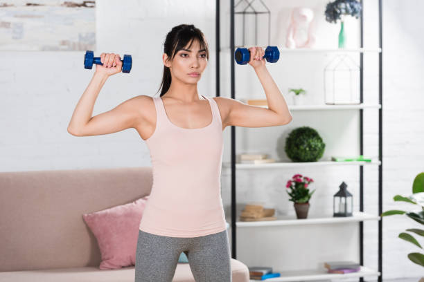 istock attractive young woman doing exercise with dumbbells at home 1005352974