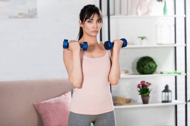istock fit young woman doing exercise with dumbbells at home 1005353006