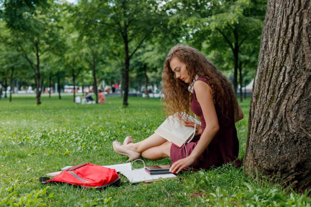 istock girl student holding book and sitting under tree 1005371988