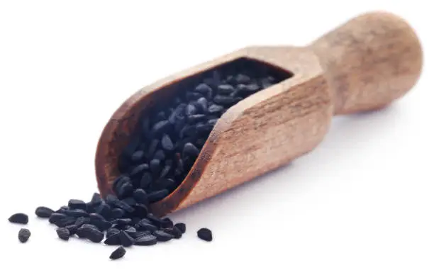 Nigella seeds in wooden scoop over white background