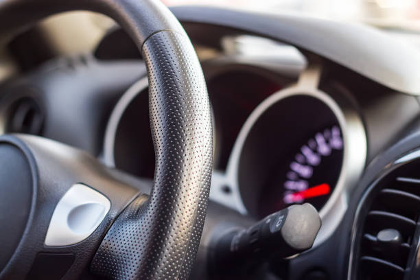 istock Close up modern black steering wheel, blurred dashboard and speedometer. Selective focus. Shallow depth of field. 1005378376