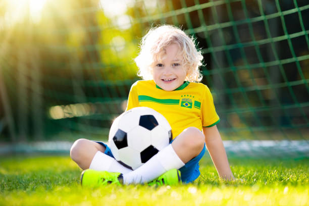 Brazil football fan kids. Children play soccer. Kids play football on outdoor field. Brazil team fans. Children score a goal at soccer game. Little boy in Brazilian jersey and cleats kicking ball. Football pitch. Sports training for player. 16286 stock pictures, royalty-free photos & images