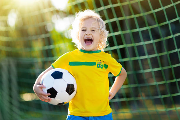 Brazil football fan kids. Children play soccer. Kids play football on outdoor field. Brazil team fans. Children score a goal at soccer game. Little boy in Brazilian jersey and cleats kicking ball. Football pitch. Sports training for player. brazil girl soccer fan stock pictures, royalty-free photos & images