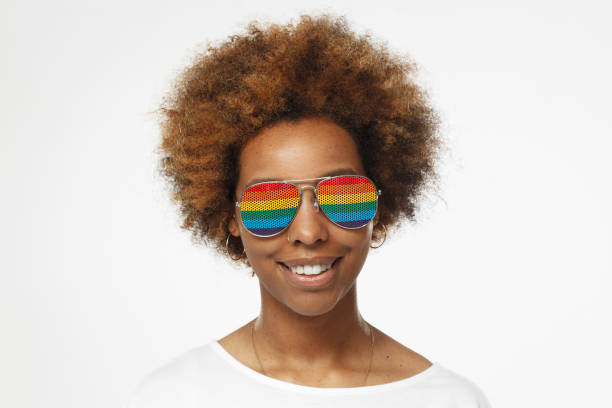 porträt des jungen afrikanerin mit schönen lächeln, regenbogen-sonnenbrille, isoliert auf grauem hintergrund hautnah - lesbian gay man rainbow multi colored stock-fotos und bilder