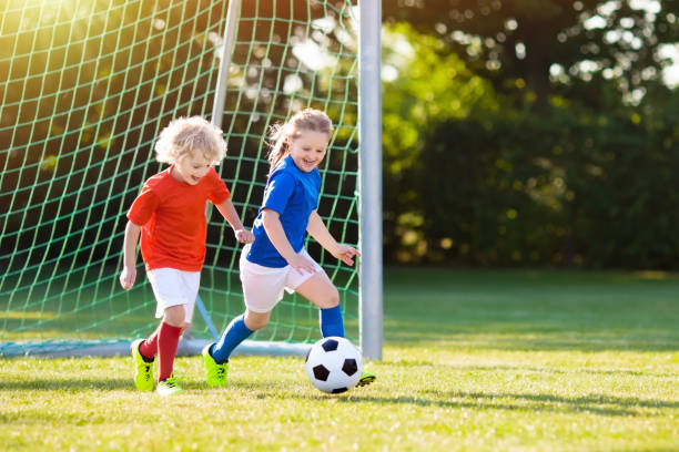 Kids play football. Child at soccer field. Kids play football on outdoor field. Children score a goal at soccer game. Girl and boy kicking ball. Running child in team jersey and cleats. School football club. Sports training for young player. sports activity stock pictures, royalty-free photos & images