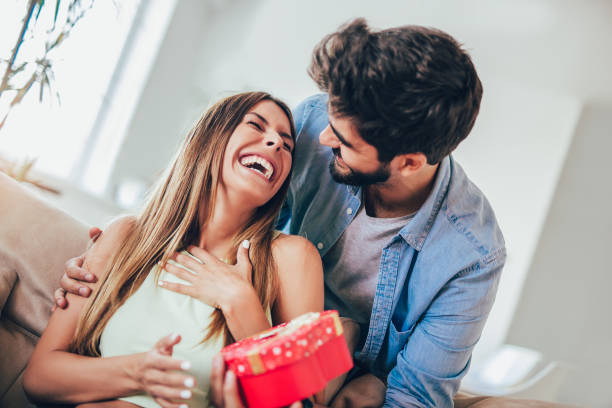 istock Smiling man surprises his girlfriend with present at home 1005390330