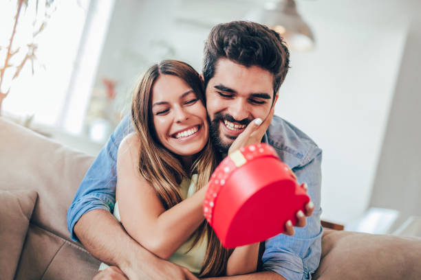 istock Smiling man surprises his girlfriend with present at home 1005390336