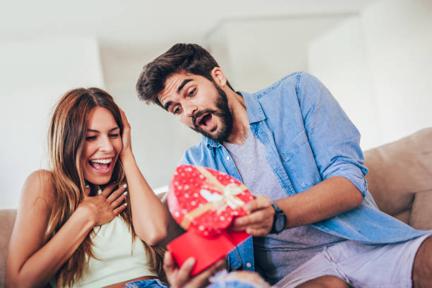 istock Smiling man surprises his girlfriend with present at home 1005390356