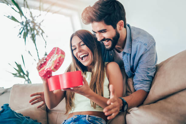 istock Smiling man surprises his girlfriend with present at home 1005390374
