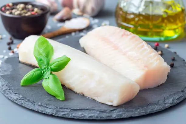 Fresh raw cod fillet with spices, pepper, salt, basil on a stone plate, horizontal