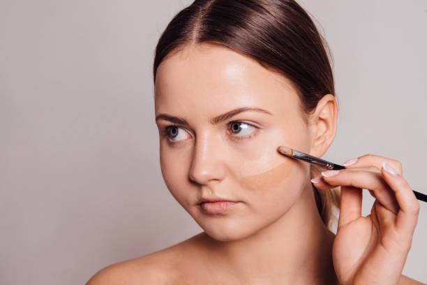 istock Young attractive girl applying cosmetic foundation with brush 1005408974