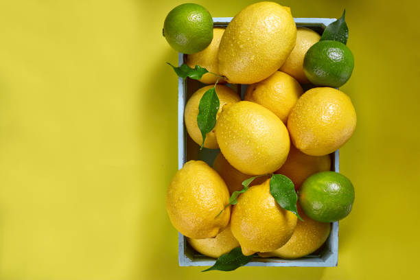 istock Box with lemons and limes and green leaves on yellow background 1005419558