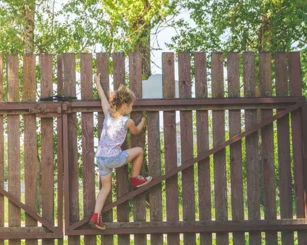 Photo of girl climbs the fence on a summer day